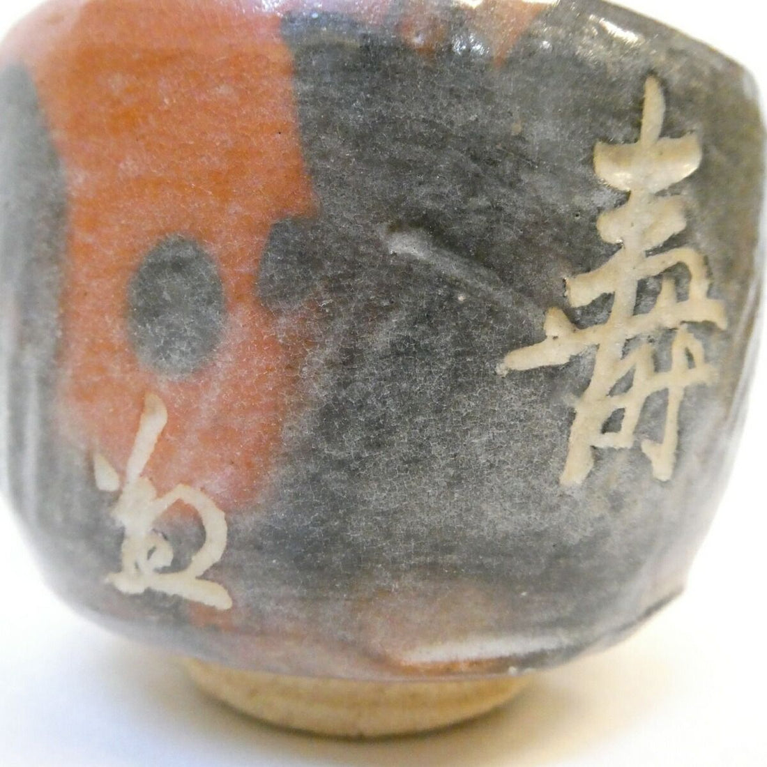 Incised character filled with white slip on the body of an aka-Raku tea bowl — an incised mark (kokumei), one of the four kinds a Japanese pot can carry