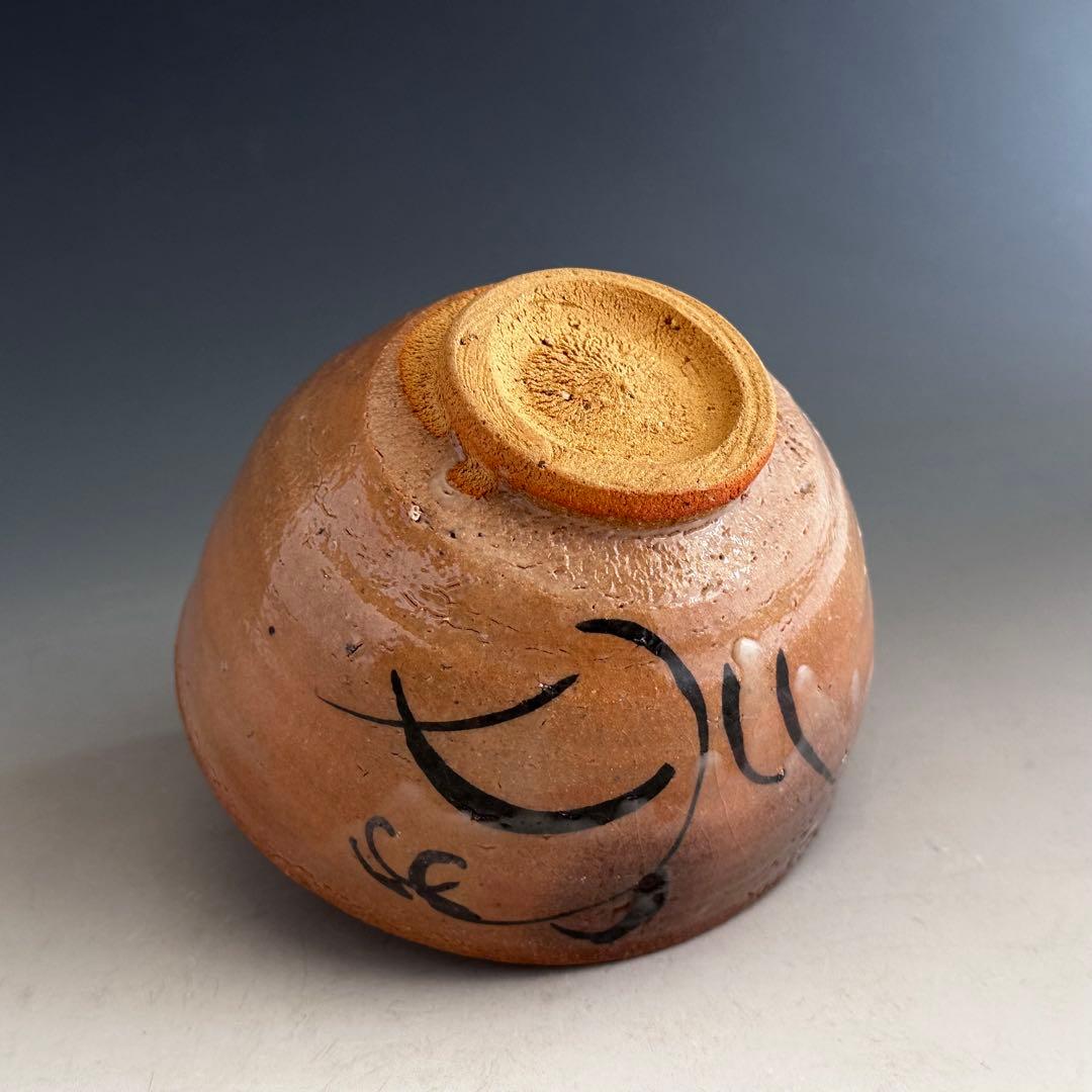 Foot of an e-Karatsu tea bowl showing bare sandy clay, throwing rings on the body and an iron-brushed grass motif — the three places a kiln is read